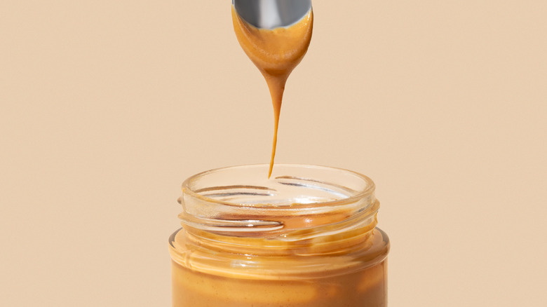 spoon with peanut butter dripping into a jar