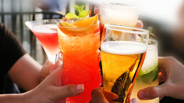 Group of people holding up glasses of various drinks, including cocktails and beer