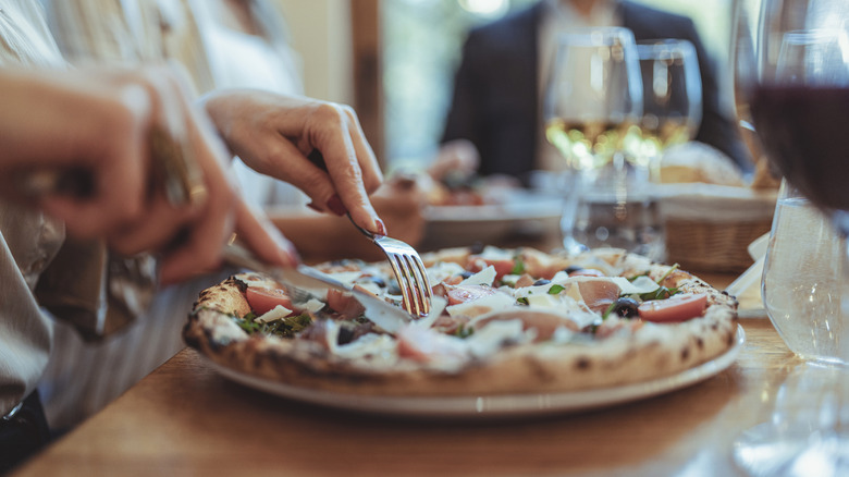 Close up of woman cutting into a pizza at a restaurant table