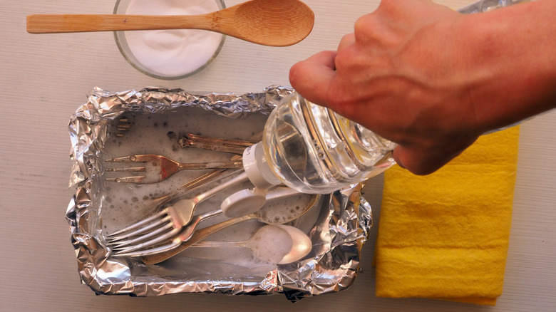 Person pouring vinegar into a container of silverware to clean it