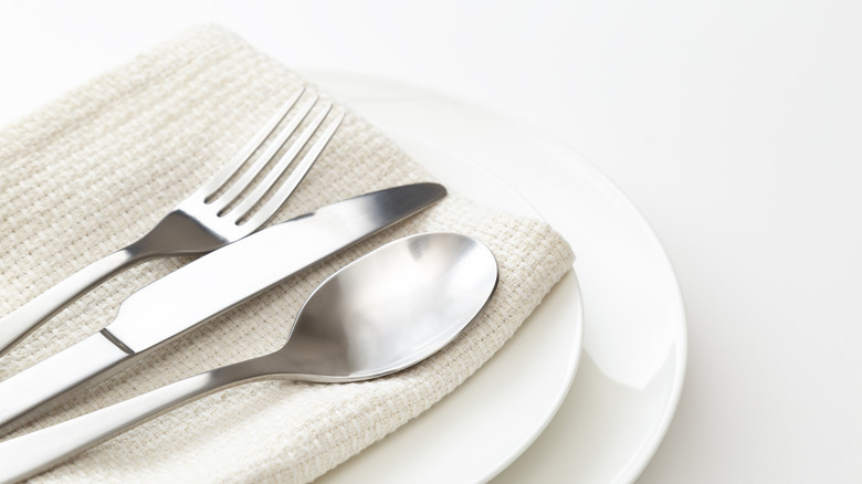 A fork, knife, and spoon on a towel on top of two white plates