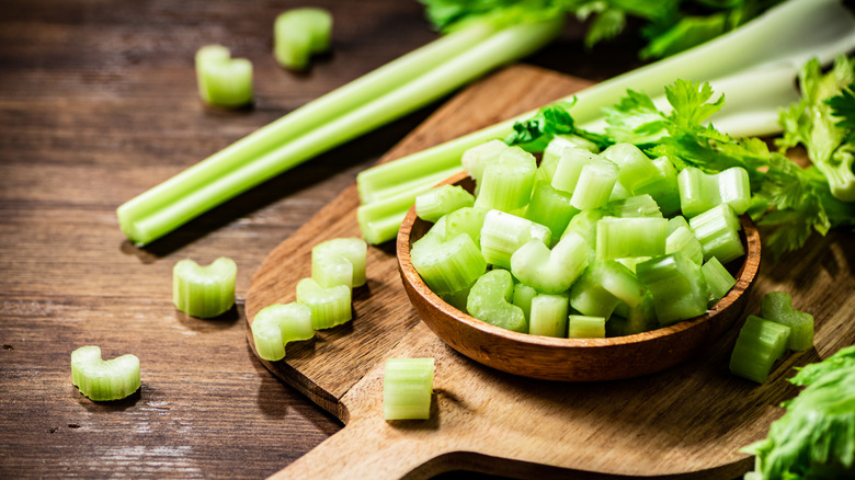 Sliced celery in a glass bowl on a cutting board.