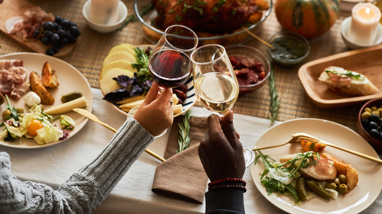 Two people clinking glasses over Thanksgiving dinner.