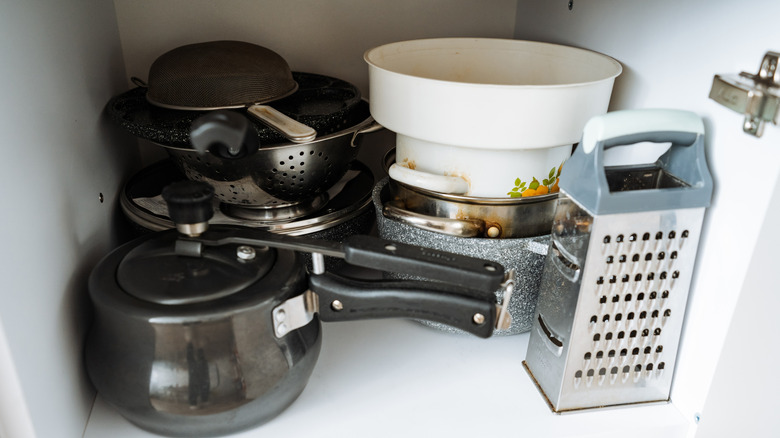 A cabinet with stacks of pans and pots plus a cheese grater to take up that awkward remaining space.
