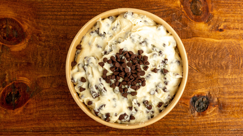 Cheesecake dip with chocolate chips in yellow bowl on brown wooden counter.