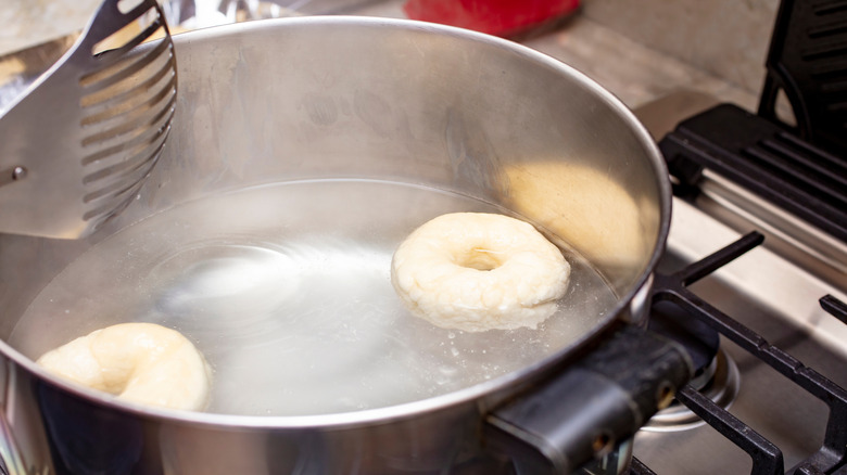 Bagel dough boiling in a pot bath on a home stove.