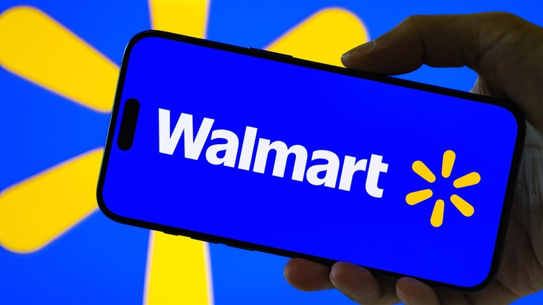 Hand holding phone with Walmart logo against a blue and yellow screen.