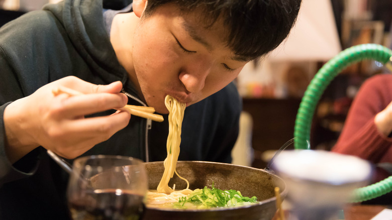young man slurping ramen noodles