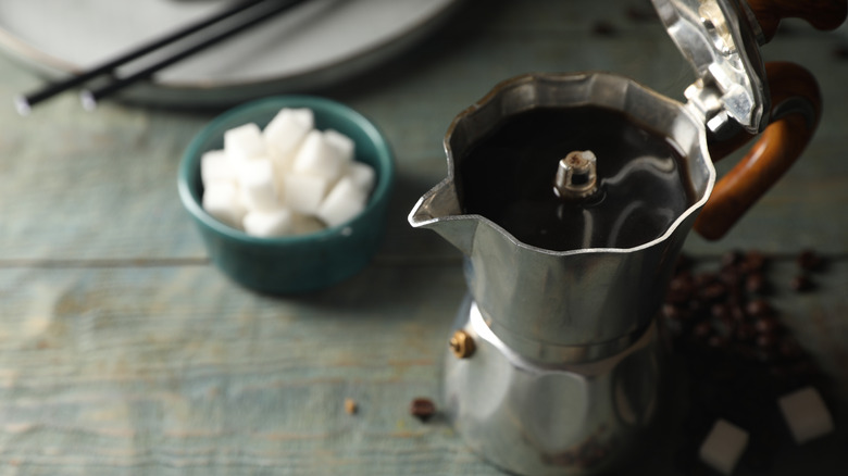 An open moka with fresh coffee inside beside a bowl of sugar cubes