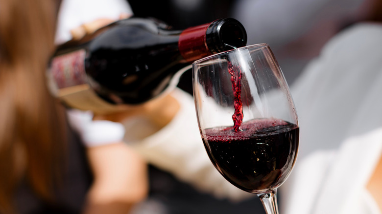 A bottle of red wine poured into glass.