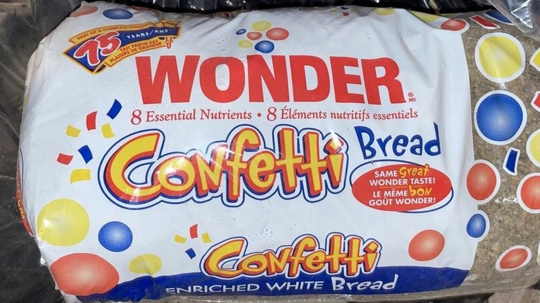 An old bag of Wonder Confetti Bread sits in the basement of a house, having been repurposed as a trash bag for used cat litter. The package features yellow, red, and blue confetti, along with the words "8 Essential Nutrients" and "Same Great Wonder Taste!" in both English and French.