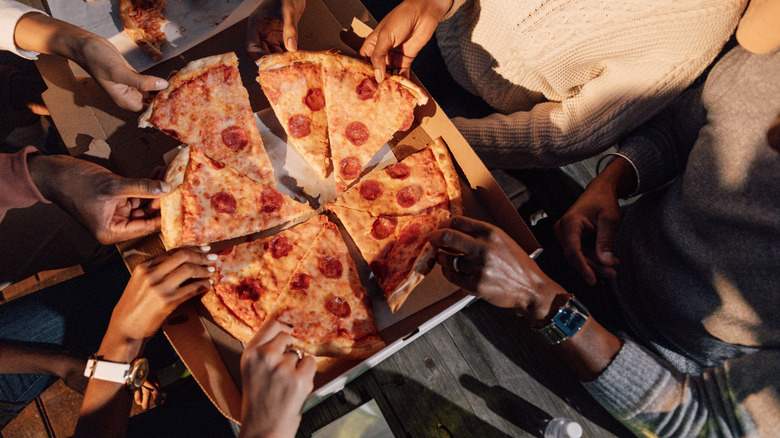 Hands grabbing slices of pizza out of a box