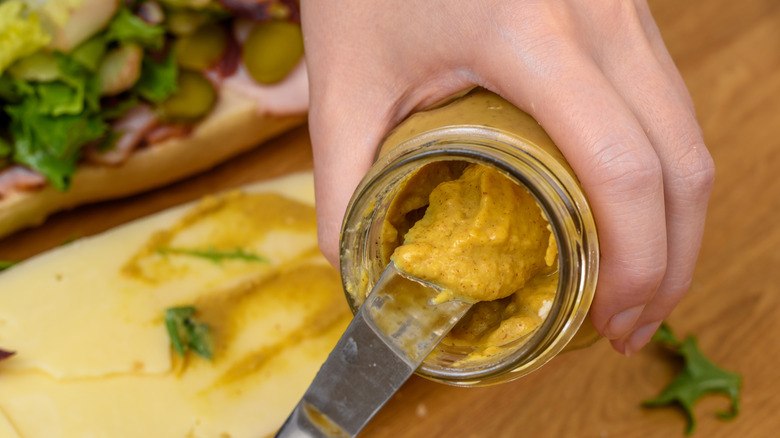 Using a knife to scoop Dijon mustard from a jar.