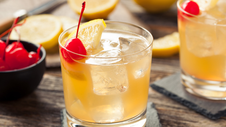 Whiskey sours garnished with lemon wedges and cherries.