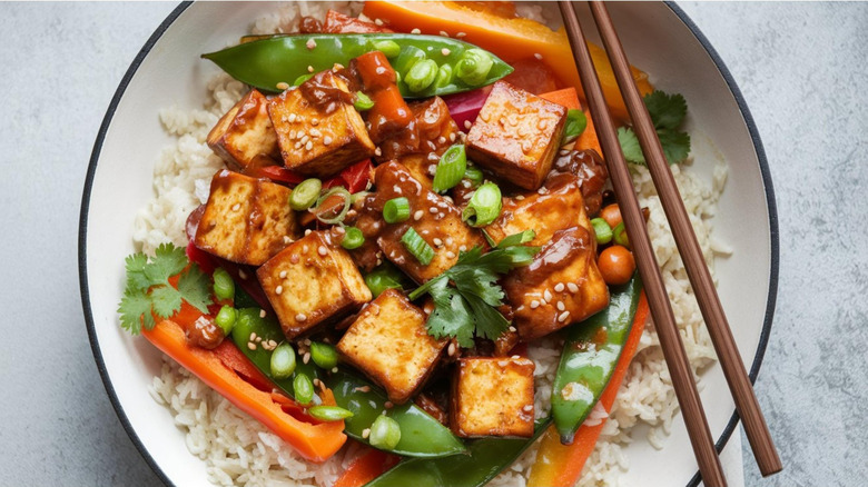 a tofu stir fry in a bowl with tofu, rice, carrots, and snap peas