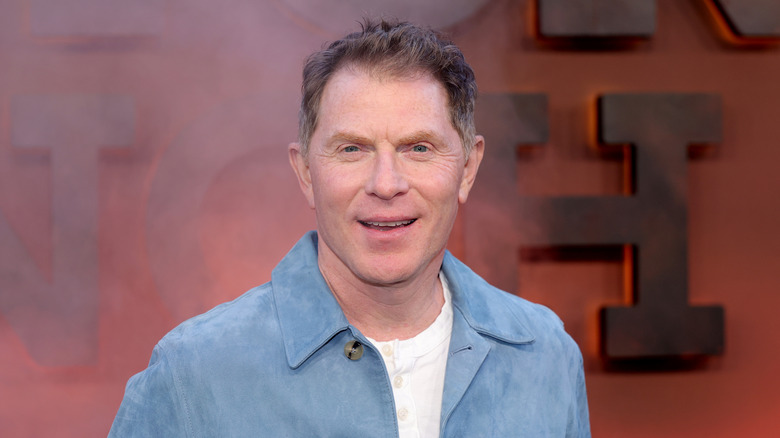 A smiling Bobby Flay wearing a blue jacket over a white shirt