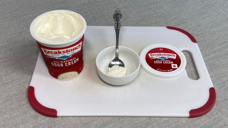 Breakstone's All Natural Sour Cream container opened with a small dollop on a spoon inside a white bowl.