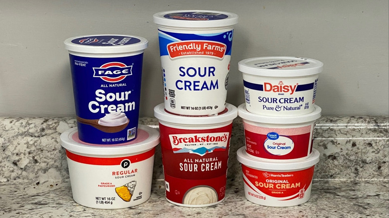 Seven sour cream brand containers stacked on a granite countertop.