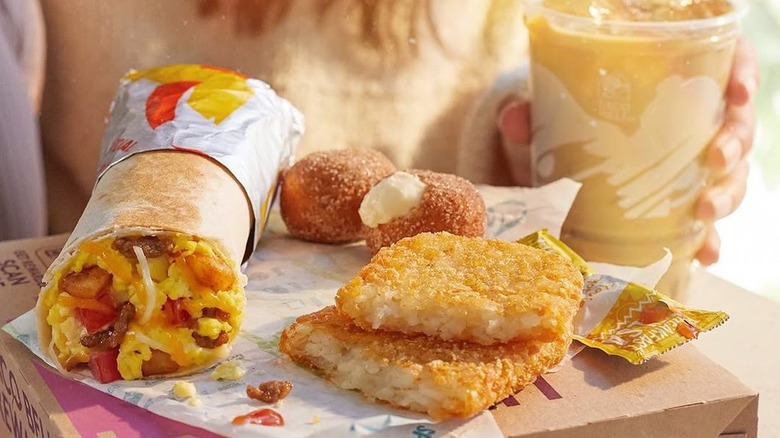 Various Taco Bell breakfast items including a burrito, hash browns, and iced coffee