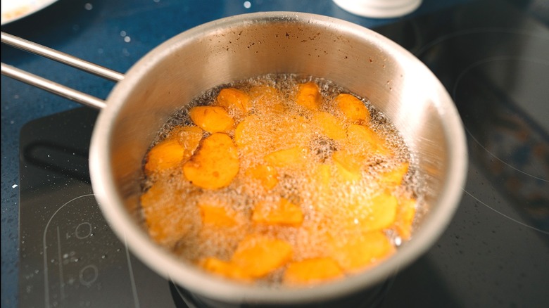 Vegetables frying in oil on a stovetop pot.