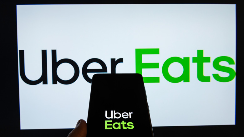 The Uber Eats logo appears on a TV screen and on a phone in a person's hand.