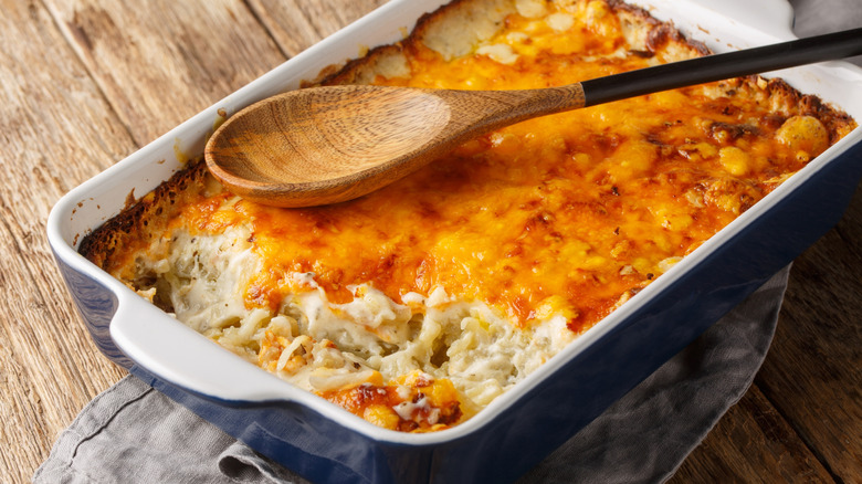 A fresh hash brown casserole dish fresh from the oven with a wooden spoon placed on top