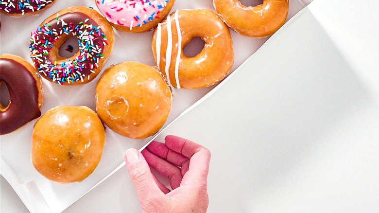 Hand touching the outside egde of a white box filled with store-bought donuts
