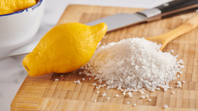 One lemon and a pile of coarse salt on a wooden cutting board.