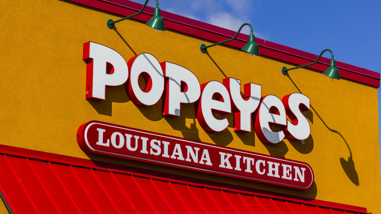 Red and white Popeyes Louisiana Kitchen sign on mustard yellow building exterior