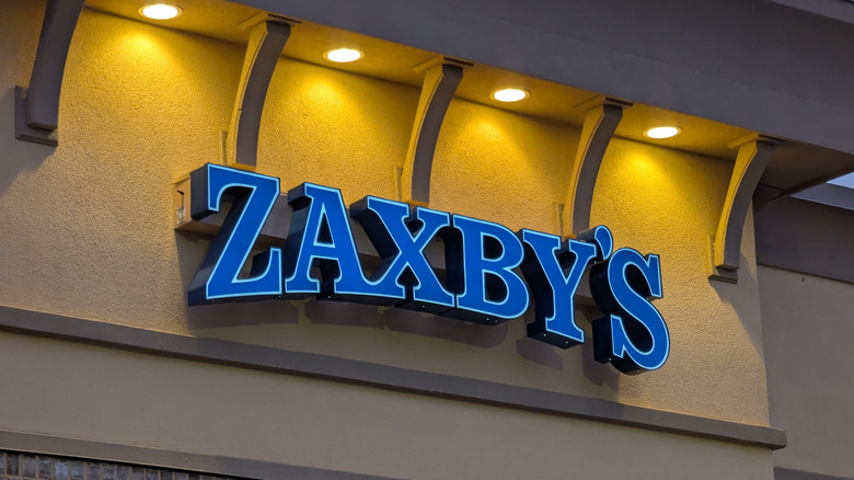Blue and white Zaxby's sign on beige stucco building beneath spot lights