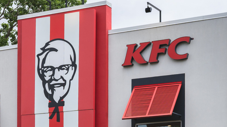 Red and black KFC logo next to red, white, and black Colonel Sanders logo on building exterior
