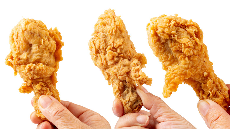 Three hands holding up pieces of deep fried chicken on white background