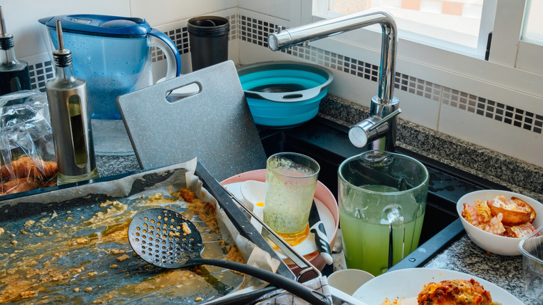 A sinkful of filthy dishes, including a blender, baking sheet, and cutting board