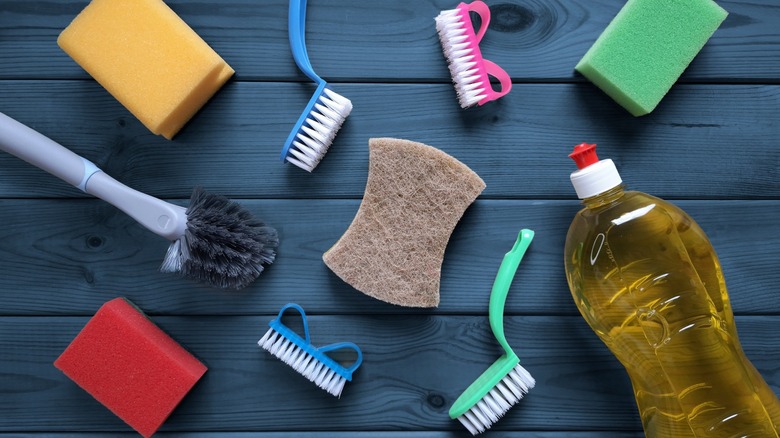 Sponges, brushes, dish liquid assortment on blue wood grain background