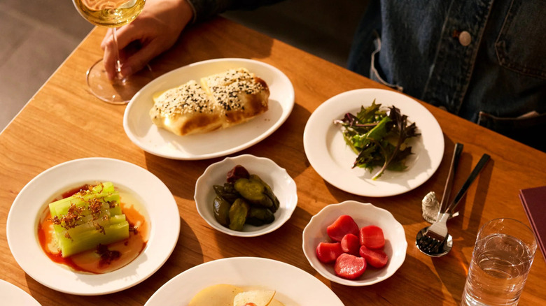A table set with small plates from Lei while a hand holds the stem of a wine glass