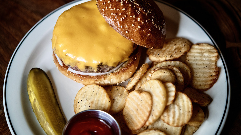 A burger from Red Hook Tavern plated with a side of potato chips and a pickle spear