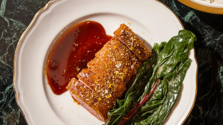 A white, gold-lined plate of food from Torrisi set atop a green marble table