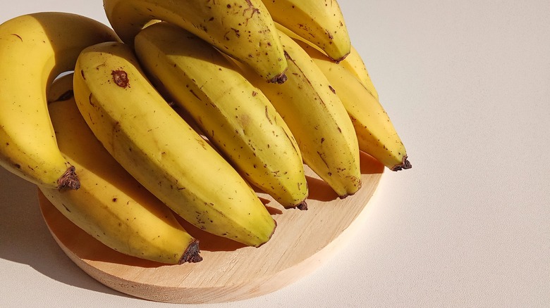 A bunch of ripe bananas sits on a round wooden board on a counter