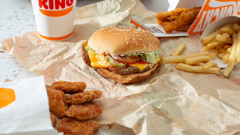 A Burger King meal with a cheeseburger, drink, chicken fries, regular fries, and chicken nuggets sitting on a to-go wrapper
