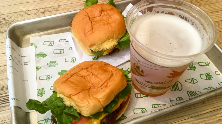 Two cheeseburgers from Shake Shack sitting on a serving tray with a beer