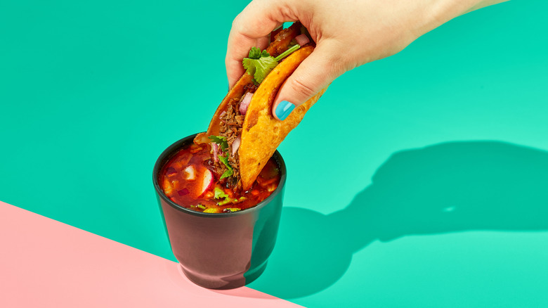 Dipping birria tacos in consumé