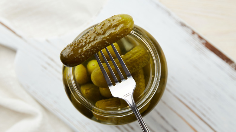A pickle on a fork held over a jar of pickles