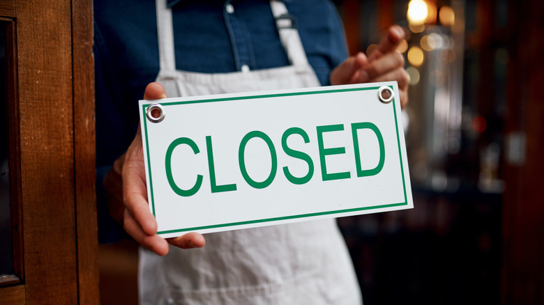 Person in apron holding up white "closed" sign in window.