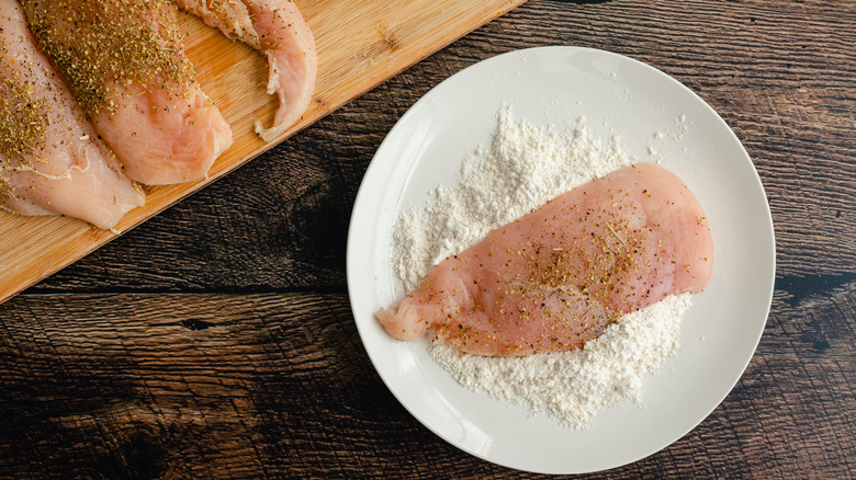 A piece of chicken sitting on top of dredging flour, seen from above.