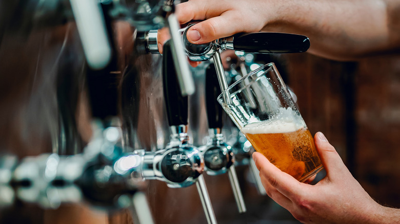 Beer being poured from the tapline into a half-full glass.