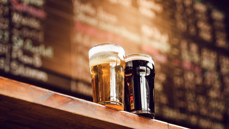 Two glasses of beer sitting on a shelf, with a blurred menu in the background.