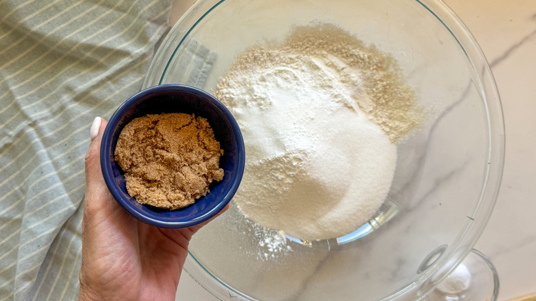 hand adding brown sugar to bowl