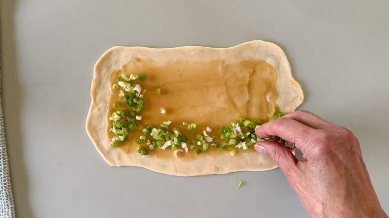 Sprinkling sliced scallions over roux on rolled out scallion pancake dough