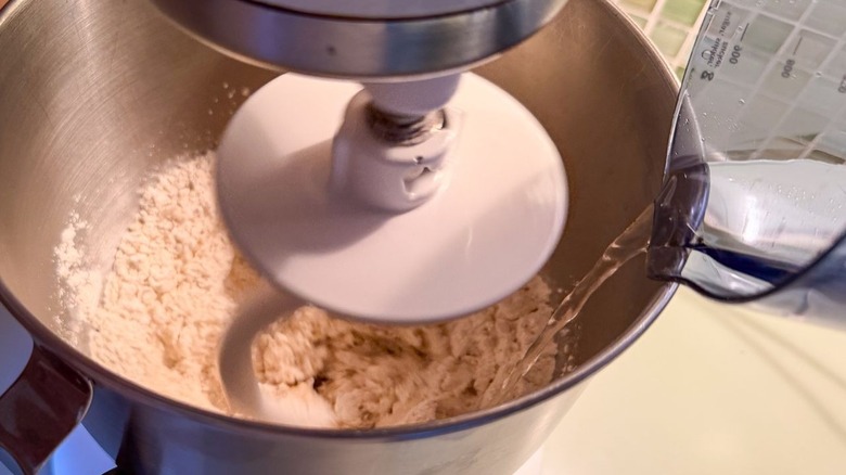 Adding hot water to stand mixer bowl with flour and dough hook