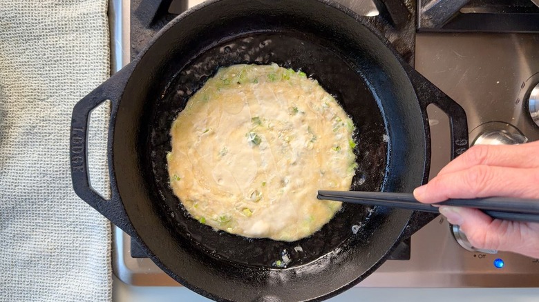 Moving a scallion pancake with chopsticks in cast iron skillet